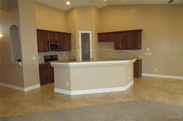 kitchen featuring a center island with sink, light countertops, stainless steel microwave, high vaulted ceiling, and baseboards