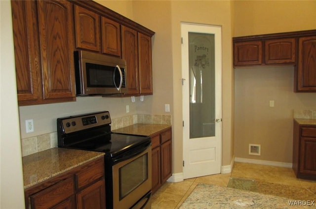 kitchen featuring light stone countertops, baseboards, stainless steel appliances, and light tile patterned flooring