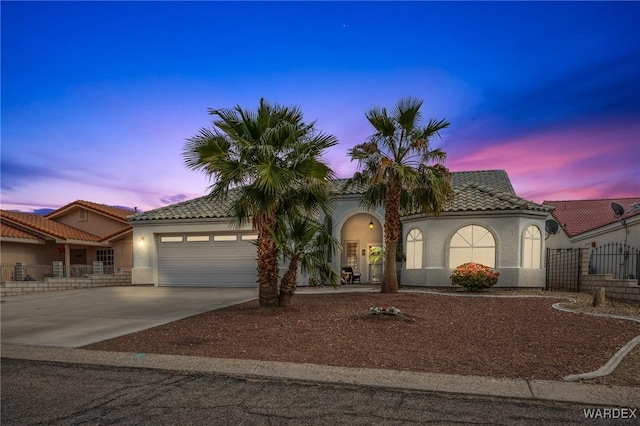 view of front facade with fence, concrete driveway, a tile roof, stucco siding, and a garage