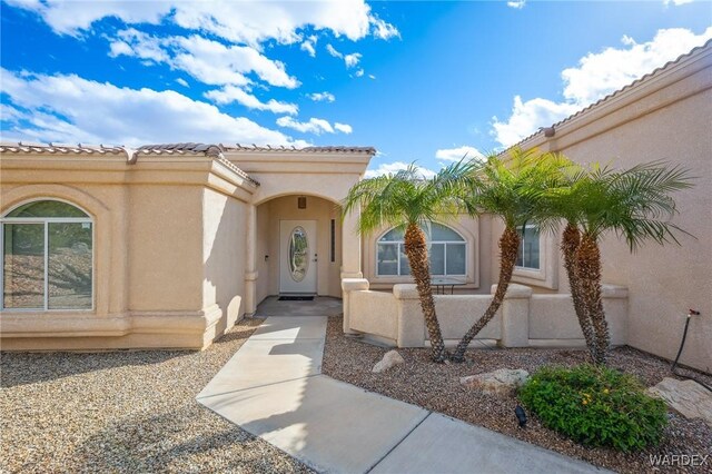 view of exterior entry featuring a tiled roof, fence, and stucco siding