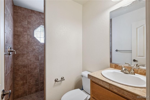 bathroom featuring tiled shower, vanity, and toilet