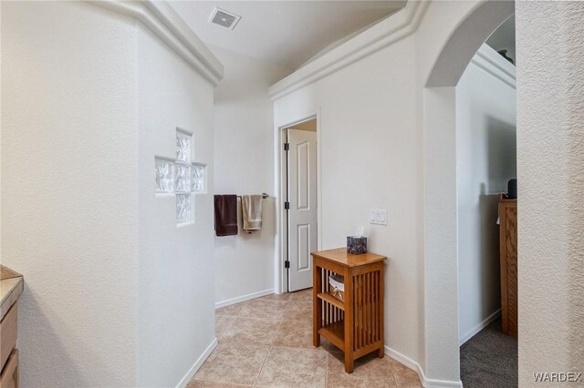 hall with light tile patterned floors, visible vents, arched walkways, and baseboards