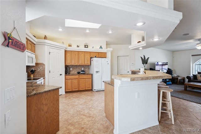 kitchen with white appliances, tasteful backsplash, a skylight, a breakfast bar area, and open floor plan