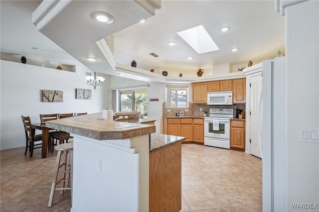 kitchen with white appliances, a skylight, visible vents, a kitchen breakfast bar, and decorative backsplash