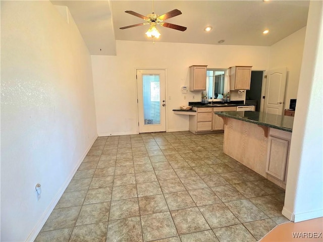 kitchen featuring dark countertops, ceiling fan, light brown cabinets, baseboards, and vaulted ceiling