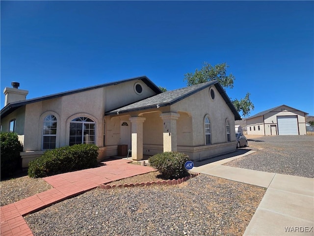 view of front of property with a detached garage, a chimney, an outbuilding, and stucco siding