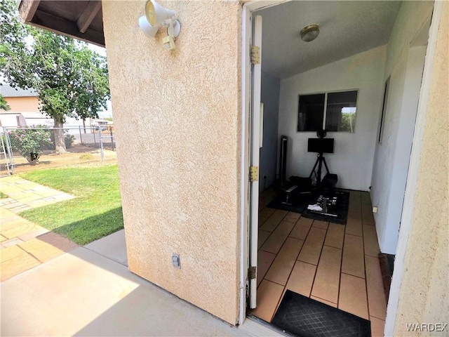 view of exterior entry with stucco siding, a yard, and fence