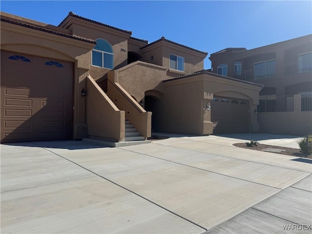 mediterranean / spanish-style home featuring a tile roof, stucco siding, a garage, driveway, and stairs