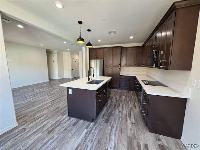 kitchen with a sink, visible vents, light countertops, a center island with sink, and pendant lighting