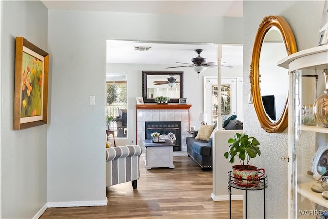 interior space featuring a fireplace, visible vents, ceiling fan, wood finished floors, and baseboards