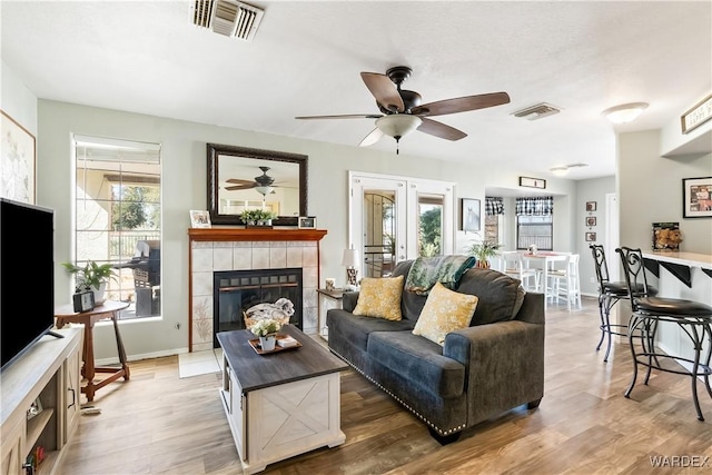 living area featuring light wood finished floors, a fireplace, visible vents, and baseboards