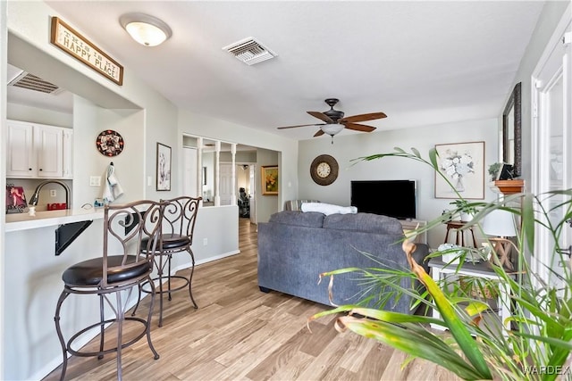 living room featuring light wood-style flooring, visible vents, and a ceiling fan