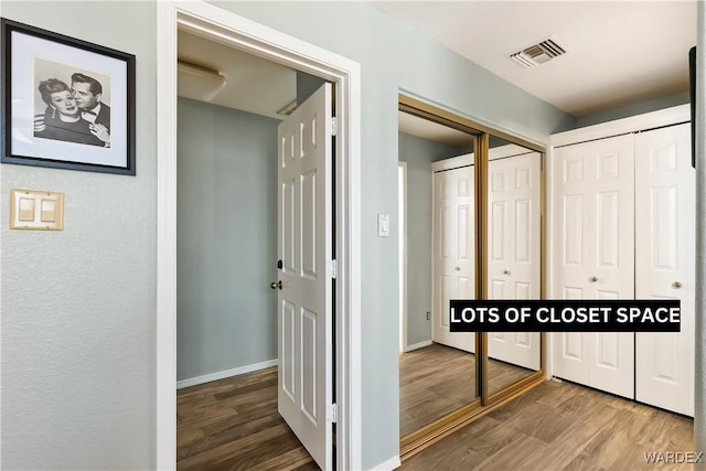 hallway with baseboards, visible vents, and wood finished floors