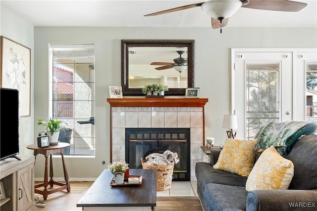 living area featuring a wealth of natural light, ceiling fan, a tiled fireplace, and wood finished floors