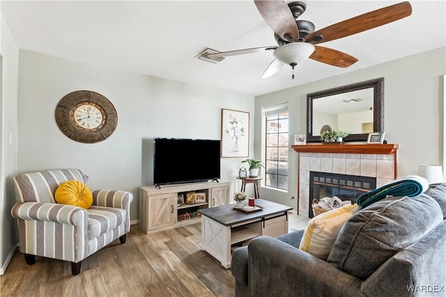 living area featuring light wood-style floors, a fireplace, and a ceiling fan