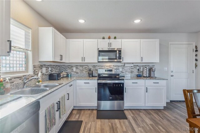 kitchen with light stone counters, appliances with stainless steel finishes, a sink, and white cabinetry