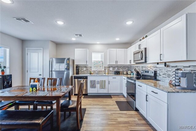 kitchen featuring visible vents, white cabinets, light wood-style flooring, appliances with stainless steel finishes, and light stone counters