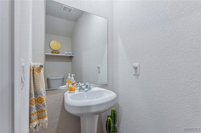 half bath with toilet, a textured wall, and visible vents