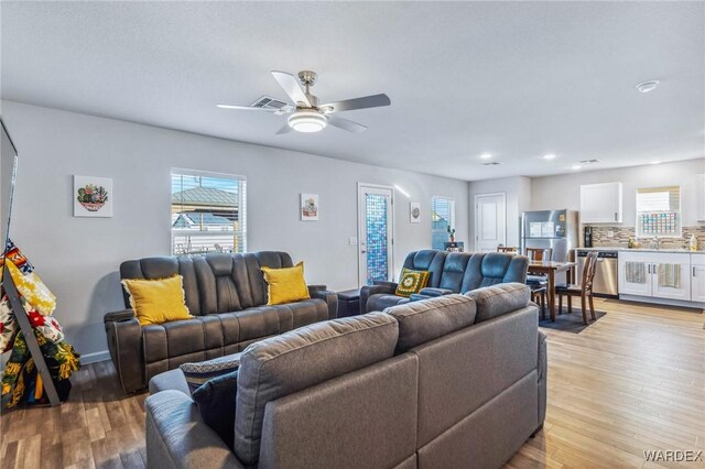 living area with a ceiling fan, visible vents, and light wood finished floors