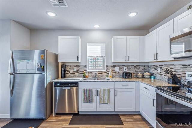 kitchen with stainless steel appliances, visible vents, white cabinetry, a sink, and wood finished floors