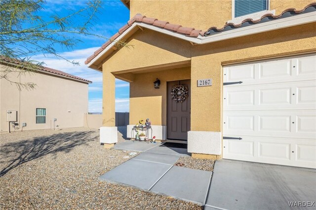 view of exterior entry featuring a garage, a tiled roof, and stucco siding