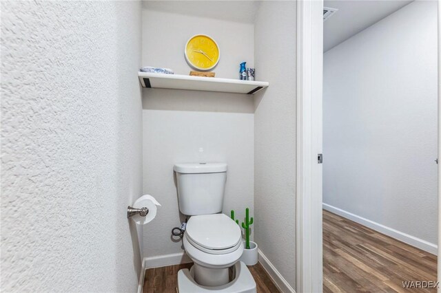 bathroom with a textured wall, toilet, wood finished floors, visible vents, and baseboards