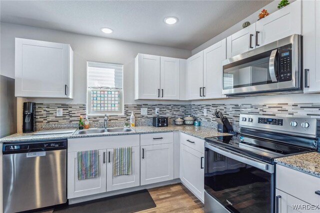 kitchen with stainless steel appliances, white cabinetry, a sink, and light stone countertops