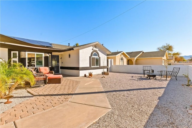 back of house with an outdoor living space with a fire pit, stucco siding, roof mounted solar panels, a patio area, and a fenced backyard