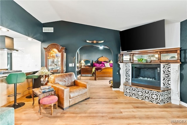 sitting room featuring arched walkways, light wood finished floors, vaulted ceiling, and a fireplace