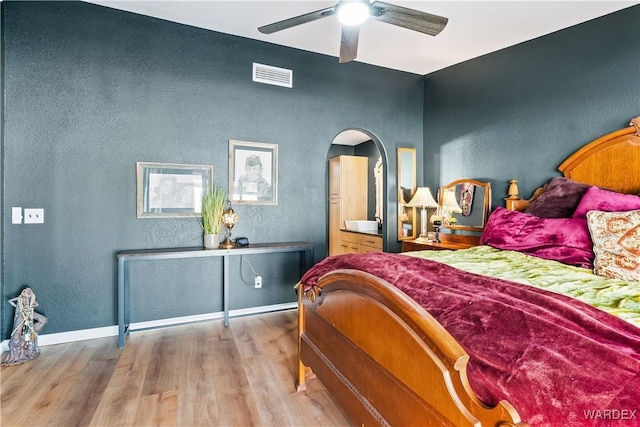 bedroom featuring arched walkways, a textured wall, visible vents, baseboards, and light wood-style floors