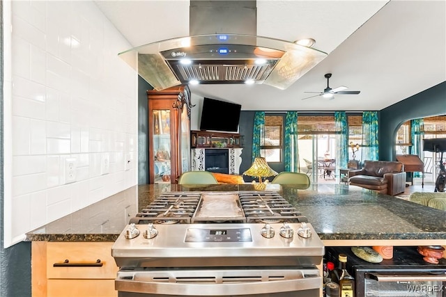 kitchen featuring a ceiling fan, open floor plan, decorative backsplash, stainless steel gas stove, and island exhaust hood