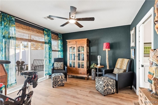 living area featuring a ceiling fan, light wood-type flooring, visible vents, and a textured wall