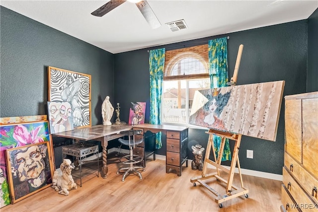 home office featuring light wood-style floors, visible vents, a textured wall, and a ceiling fan