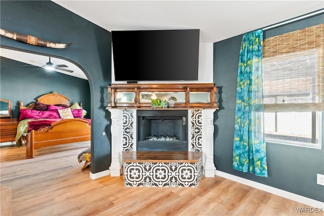 sitting room with arched walkways, a fireplace, a ceiling fan, wood finished floors, and baseboards