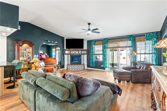 living area featuring lofted ceiling, a ceiling fan, light wood-style floors, floor to ceiling windows, and a tiled fireplace