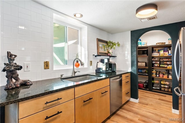 kitchen featuring visible vents, dark stone counters, appliances with stainless steel finishes, light wood-style floors, and a sink