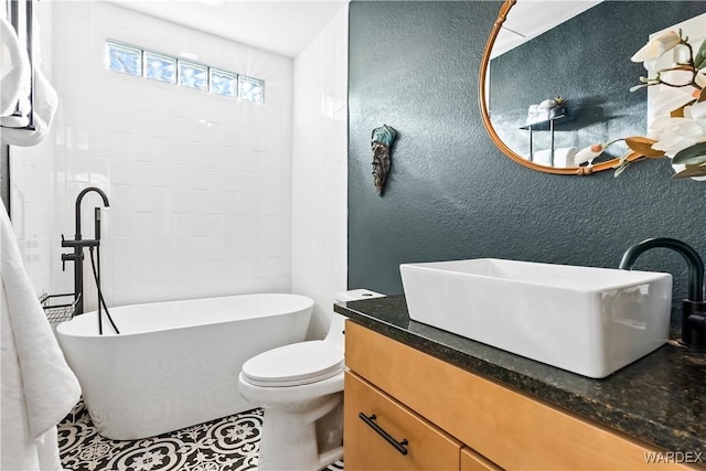 bathroom featuring a textured wall, a soaking tub, vanity, and toilet