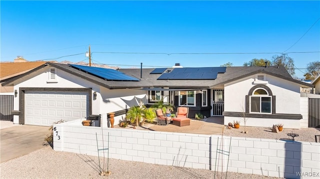 ranch-style house featuring a fenced front yard, an attached garage, concrete driveway, roof mounted solar panels, and stucco siding