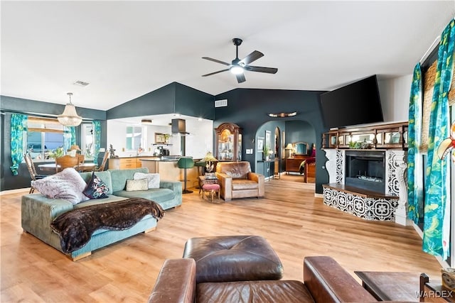 living area with arched walkways, ceiling fan, a fireplace with raised hearth, wood finished floors, and visible vents