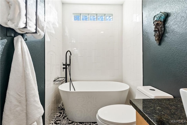 bathroom with a textured wall, a freestanding bath, vanity, and toilet