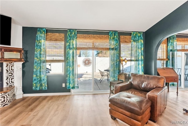 sitting room with arched walkways, baseboards, a fireplace with raised hearth, and wood finished floors