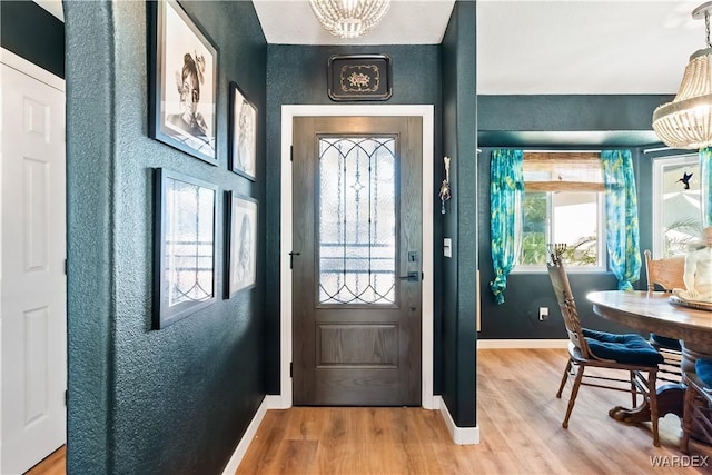 doorway to outside featuring an inviting chandelier, light wood-style flooring, baseboards, and a textured wall