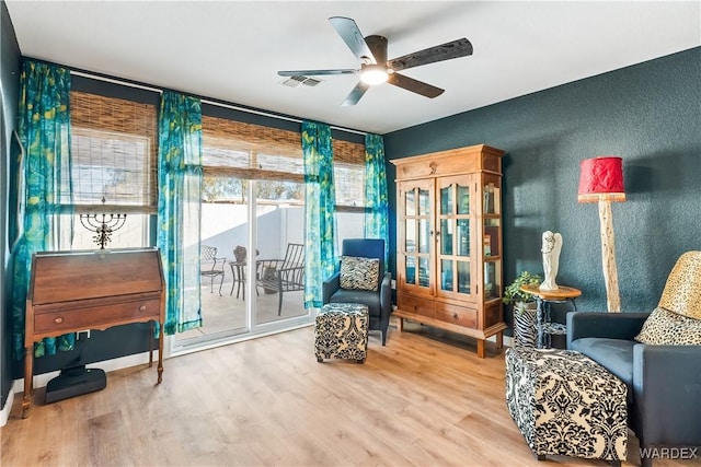 living area featuring a ceiling fan, visible vents, a textured wall, and wood finished floors