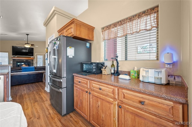 kitchen with a ceiling fan, freestanding refrigerator, light wood-style floors, a glass covered fireplace, and open floor plan