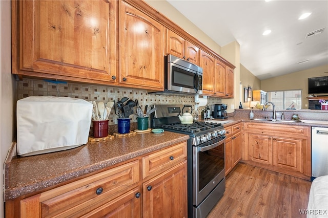 kitchen with light wood finished floors, visible vents, vaulted ceiling, stainless steel appliances, and a sink