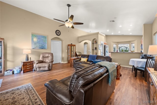 living area with visible vents, wood finished floors, arched walkways, ceiling fan, and vaulted ceiling