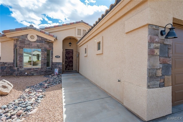 doorway to property featuring a tile roof, stone siding, and stucco siding