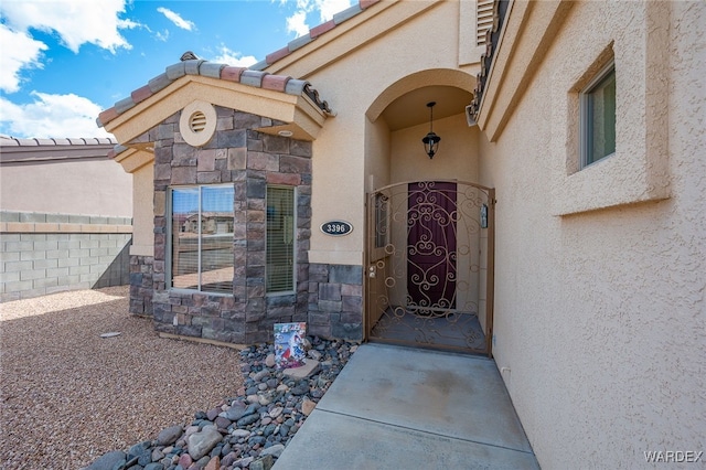 entrance to property with stone siding, stucco siding, a tile roof, and fence