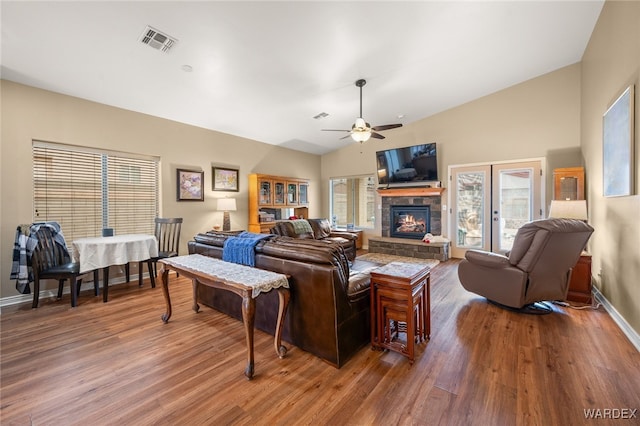 living area with visible vents, wood finished floors, a fireplace, lofted ceiling, and ceiling fan