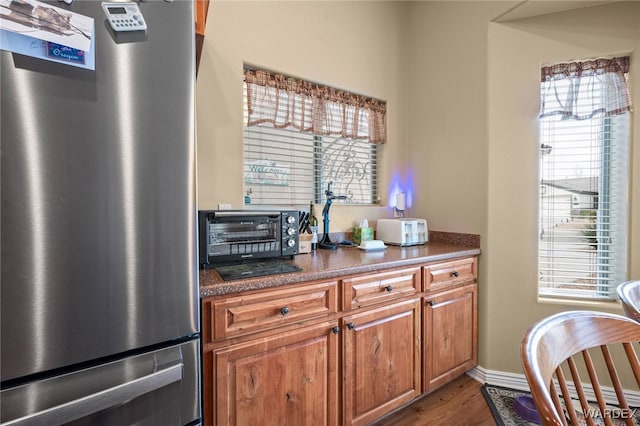 kitchen with dark wood-style floors, baseboards, a toaster, freestanding refrigerator, and brown cabinets